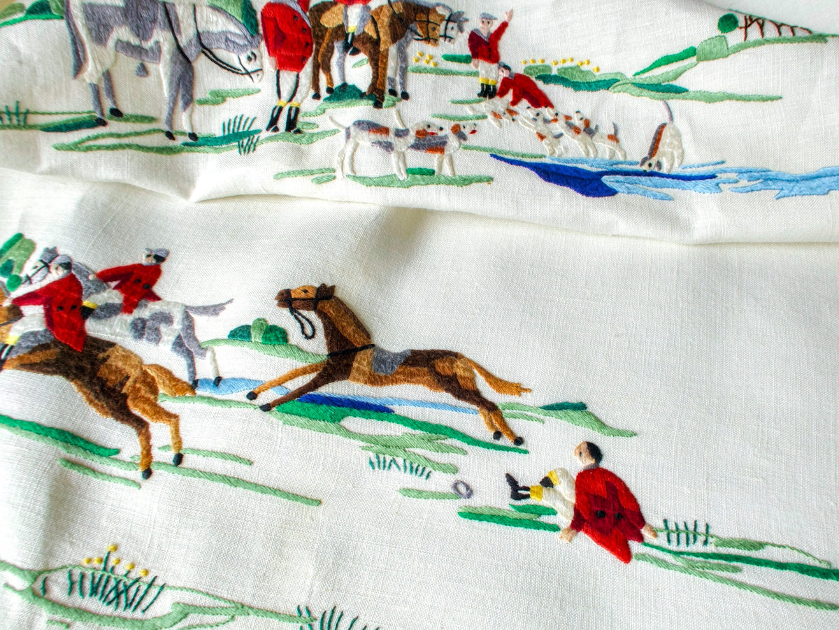 Vintage Madeira tablecloth with hand embroidered scenes of a thrown rider on the ground beside a riderless galloping horse and huntsmen waving by a stream