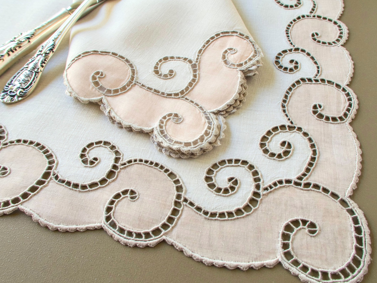 Vintage Marghab napkin corner with pink organdy appliqué scrolls resting on an "Open Scroll" placemat beside silver-handled flatware