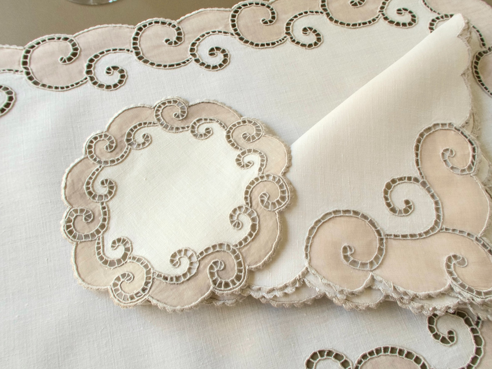 Close view of a vintage Marghab coaster beside a napkin corner, showing the hand embroidered Richelieu scrollwork and caseado bastido edging