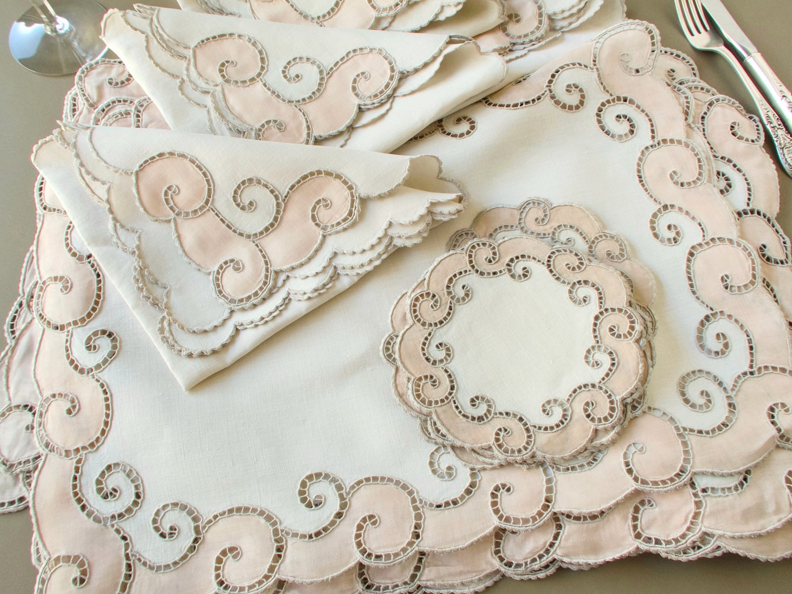 Stacked vintage Marghab placemats, napkins and a coaster showing the hand embroidered scroll borders and scalloped edges
