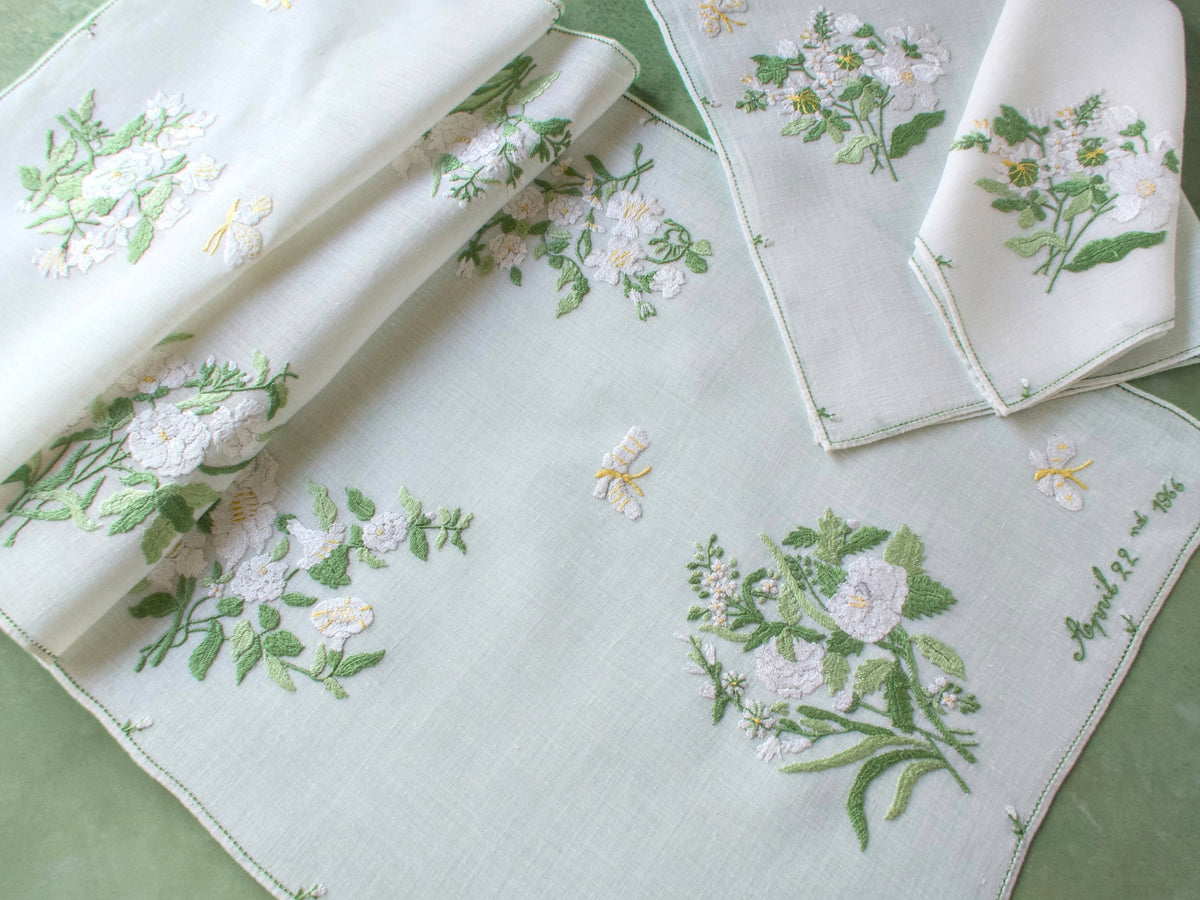 Rapisardi runner and placemats layered over green background showing semi-sheer linen and varied floral motifs.