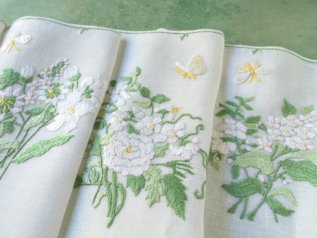 Vintage Rapisardi placemats with white floral embroidery and yellow butterflies on semi-sheer linen, displayed over green background.
