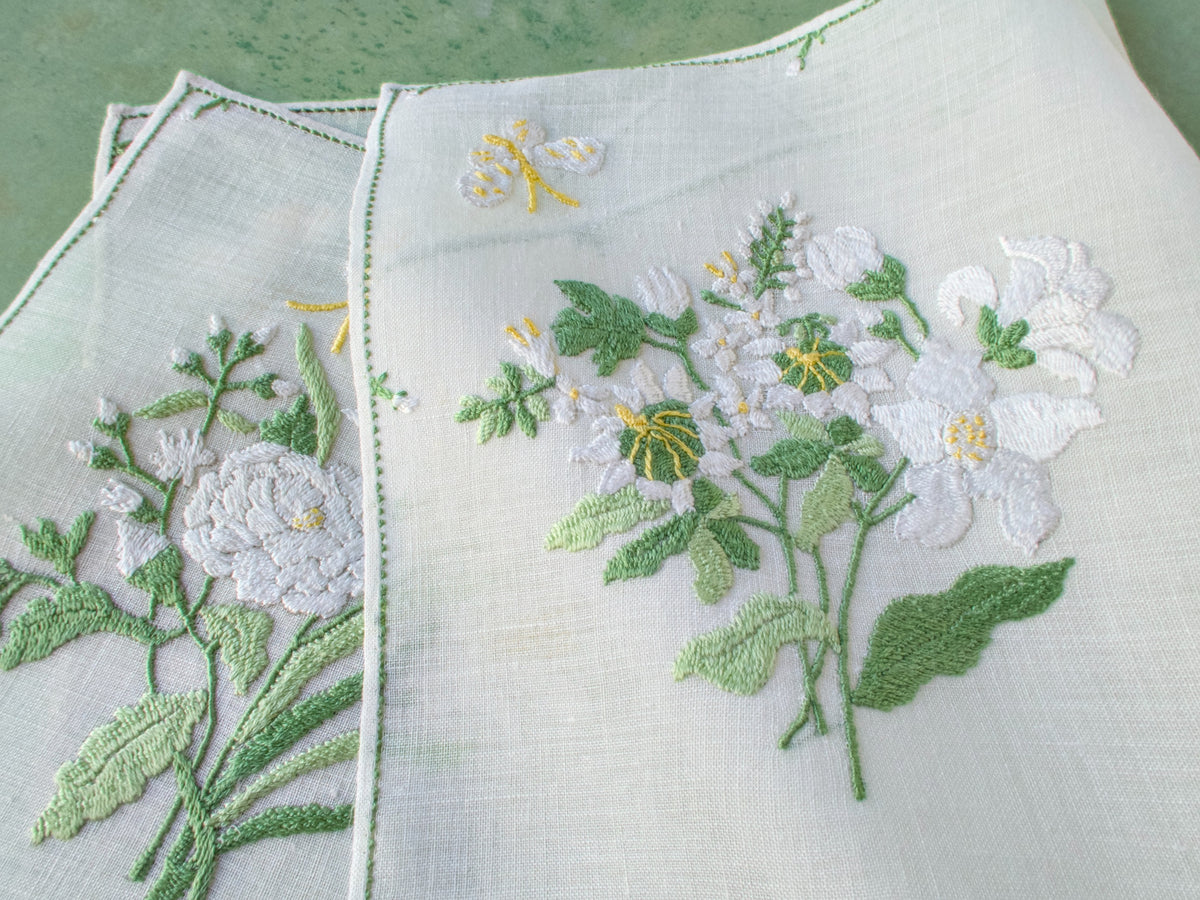 Close-up of white floral embroidery with yellow-accented blossoms and butterfly on semi-sheer linen.