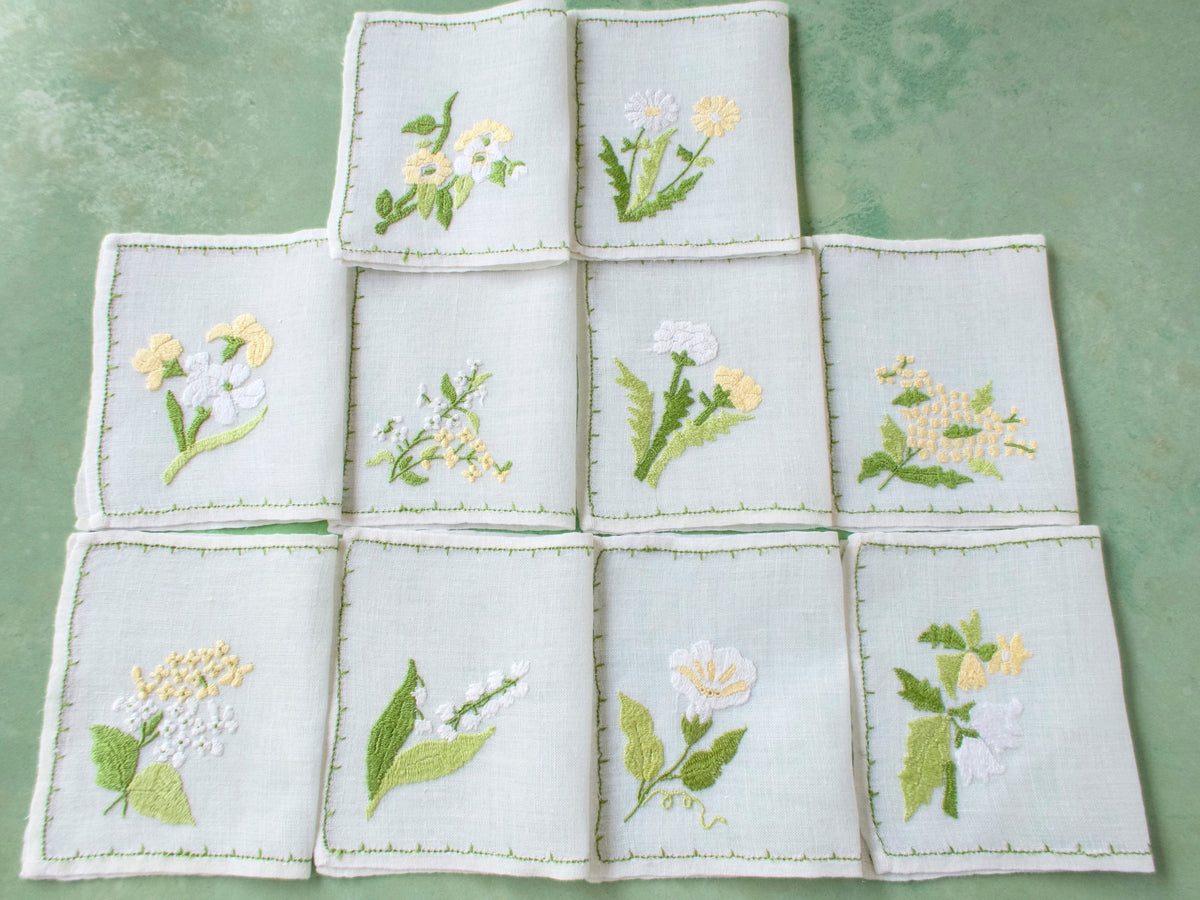 Set of 10 Baroness Rapisardi cocktail napkins, each with a different yellow and white flower, arranged in a grid on pale green background.