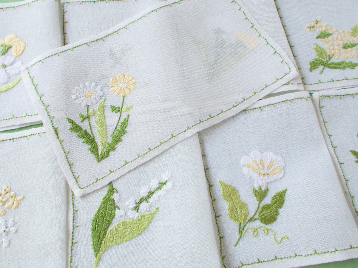 Overlapping Rapisardi linen cocktail napkins showing rectangular shape, semi-sheer weave and varied floral motifs.