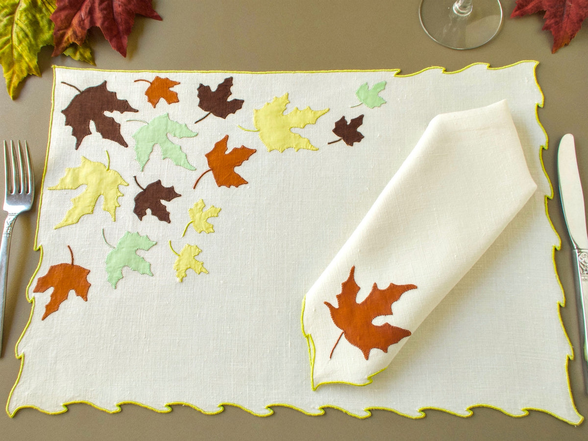 Vintage Marghab "Autumn Leaves" placemat with scattered appliqué leaves in rust, brown and chartreuse, a folded napkin showing a single rust leaf, and a silver fork