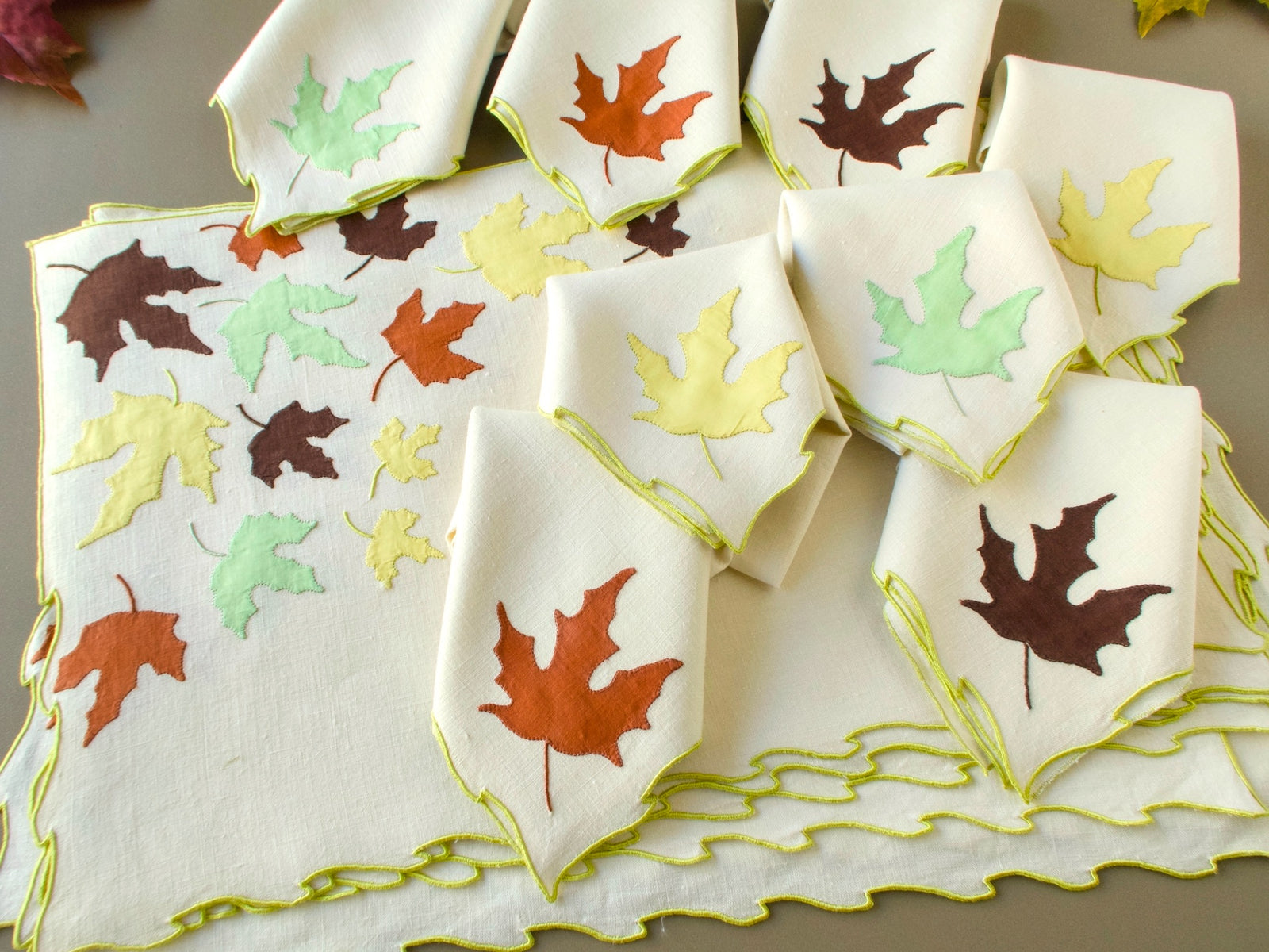 Vintage Marghab "Autumn Leaves" napkins fanned out, each with a single appliqué leaf and chartreuse edging, in front of a placemat