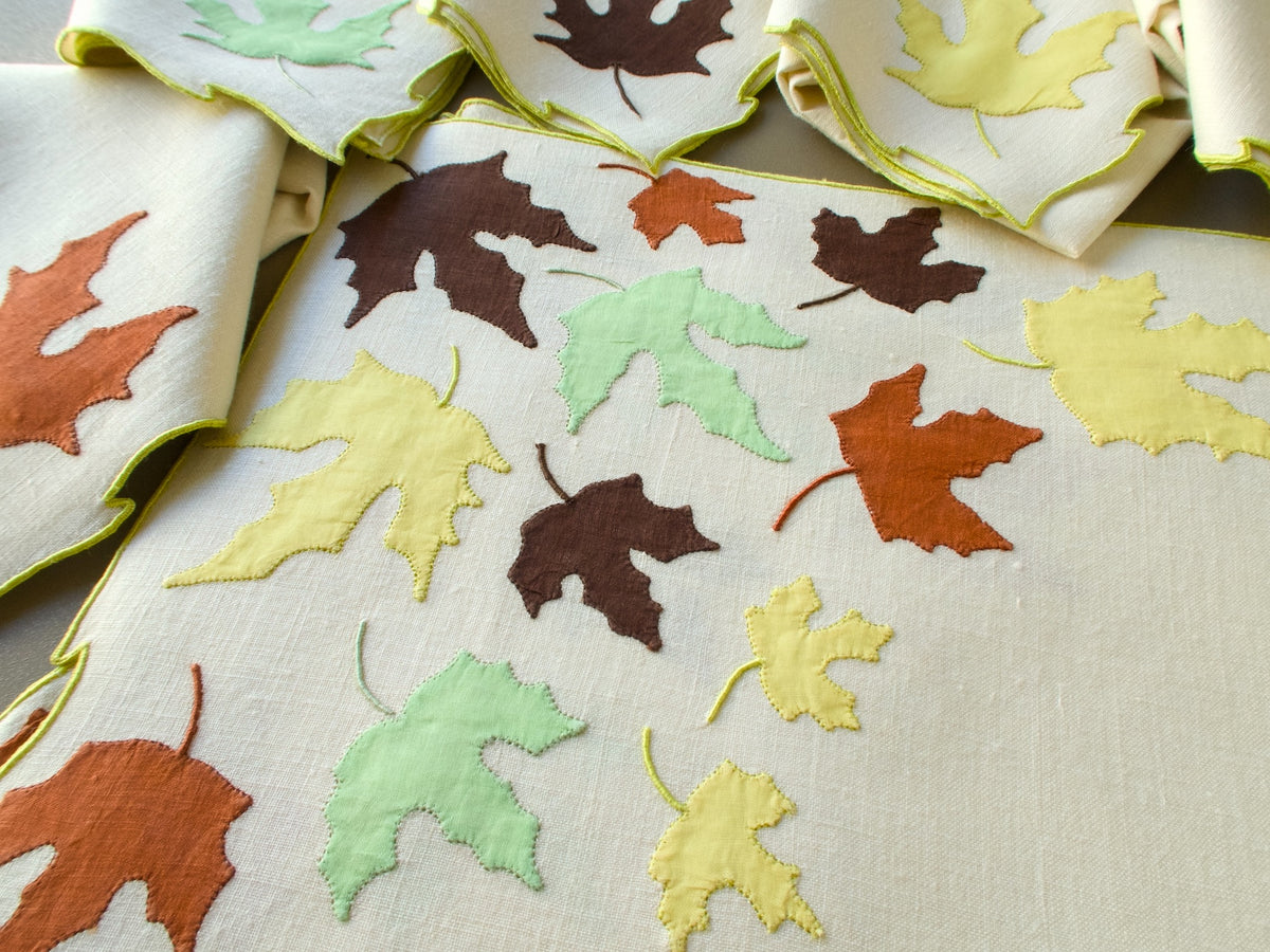 Close view of a vintage Marghab "Autumn Leaves" placemat with a drift of appliqué leaves and napkins above