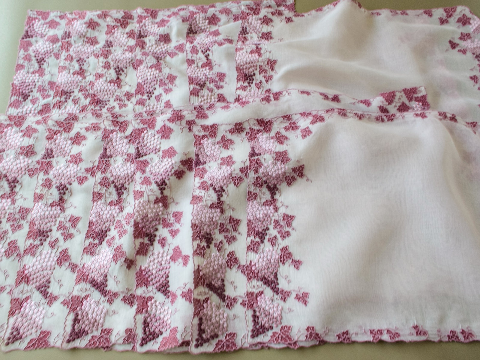 Two rows of vintage Marghab Vineyard placemats spread flat, showing grapes and leaves along the sides and sheer organdy