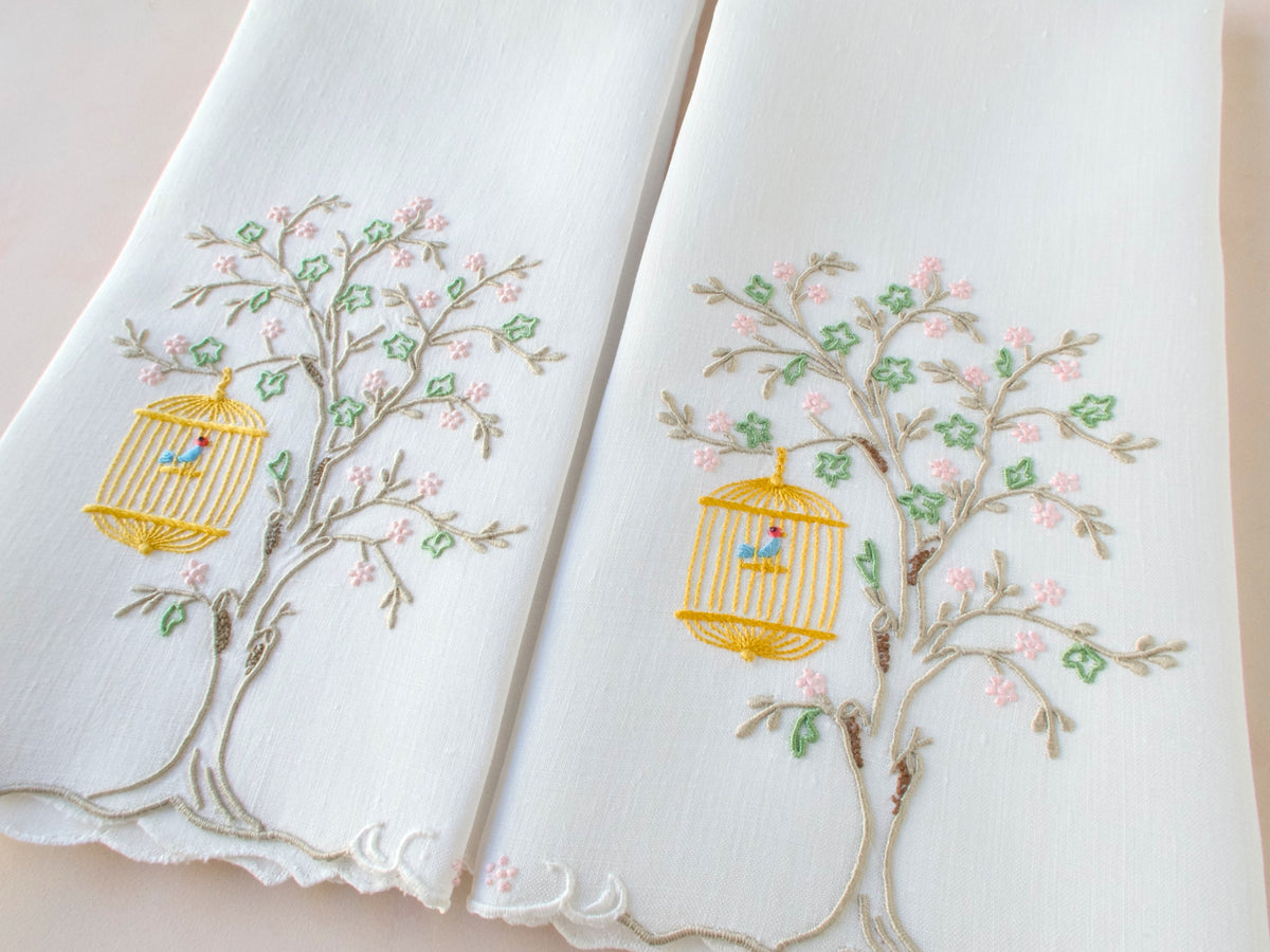 Vintage linen guest towels hand embroidered in Madeira with bird in hanging cage beneath flowering branch.