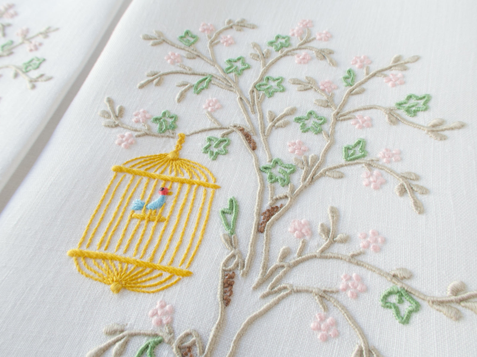 Vintage linen guest towel hand embroidered in Madeira with bird in hanging cage beneath flowering branch.