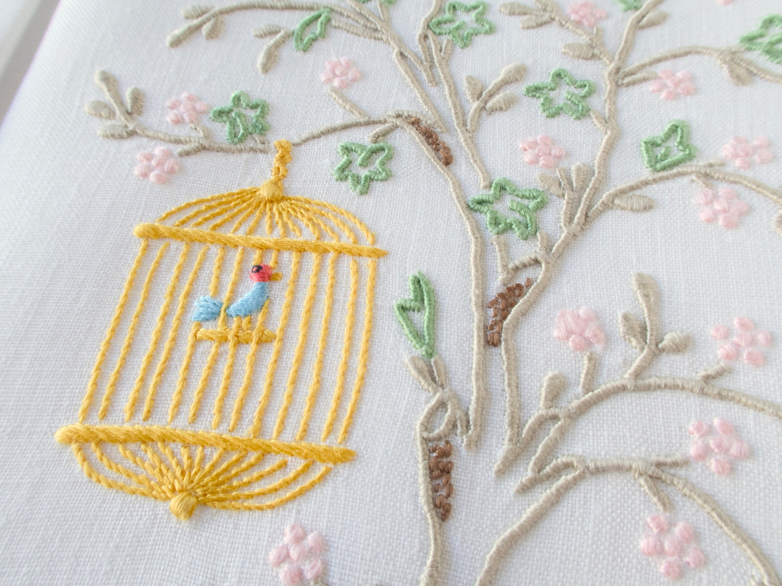 Vintage linen guest towel hand embroidered in Madeira with bird in hanging cage beneath flowering branch.