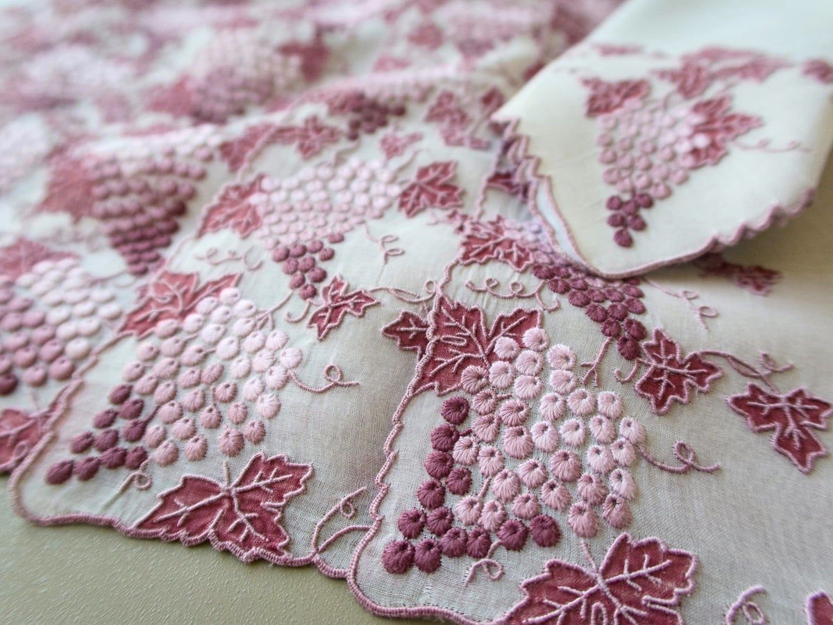 Close view of a vintage Marghab Vineyard placemat with hand embroidered pink and burgundy grape clusters and organdy appliqué leaves