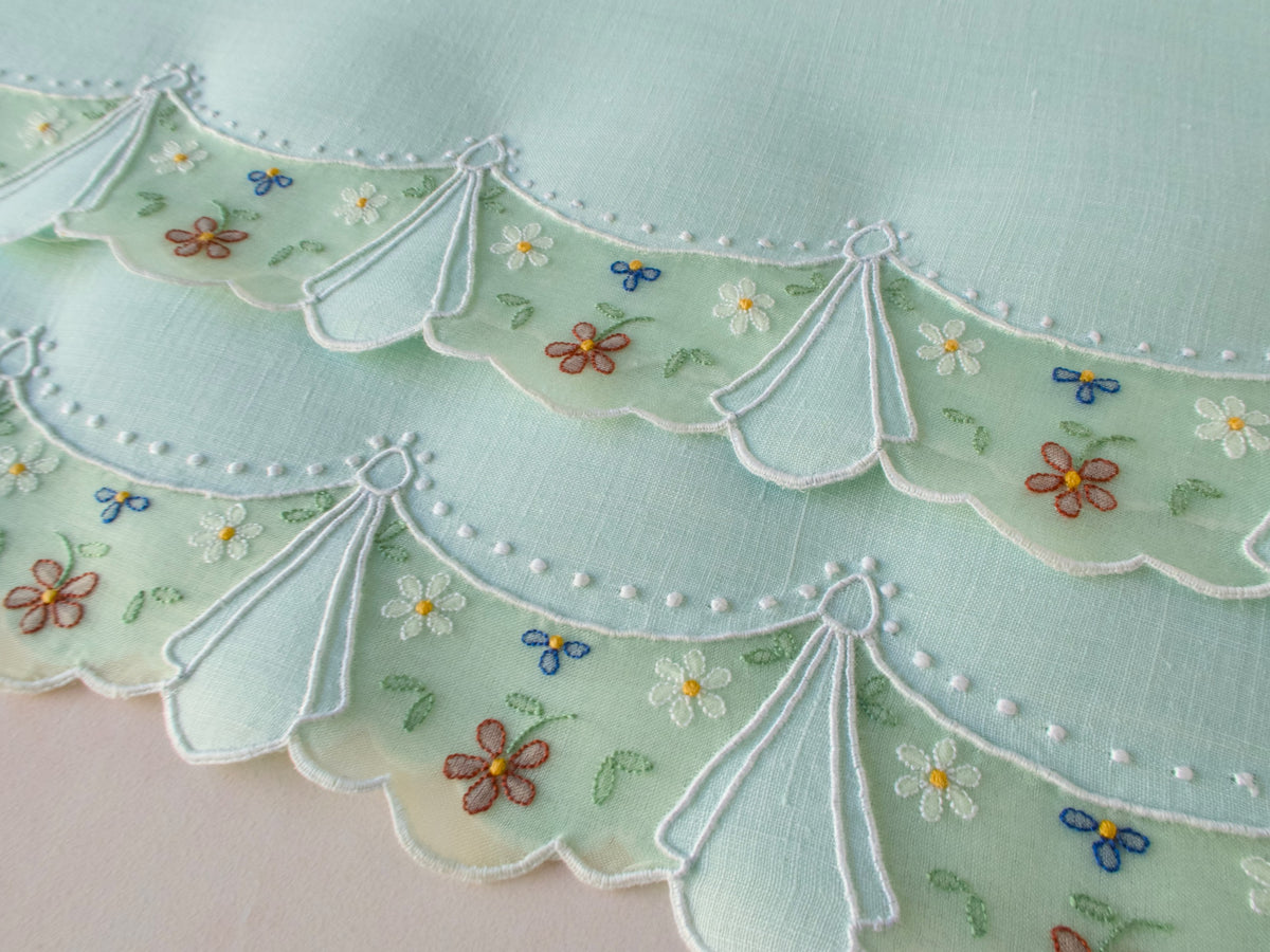 Close-up of vintage Madeira guest towel in soft green hand embroidered with organdy swag border, linen panels and scattered tiny colorful flowers