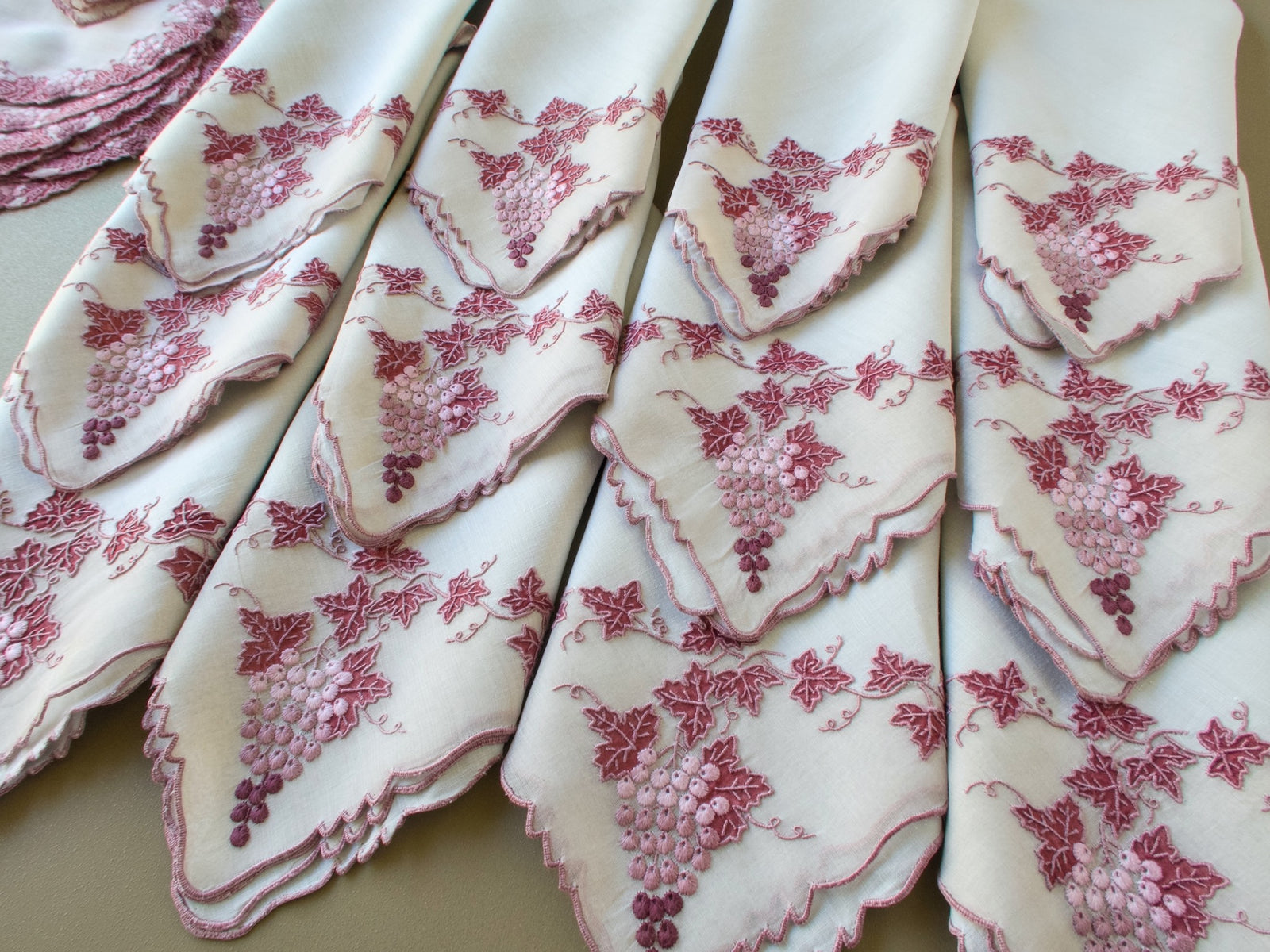 Row of vintage Marghab Vineyard linen napkins fanned out to show each hand embroidered grape corner