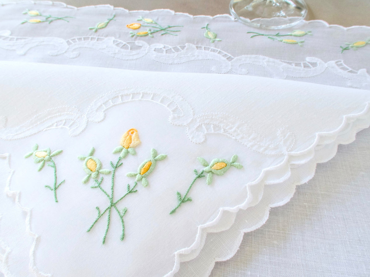 Vintage Madeira linen and organdy placemat with yellow rosebud embroidery on green stems and delicate scalloped edge, with wine glass in background