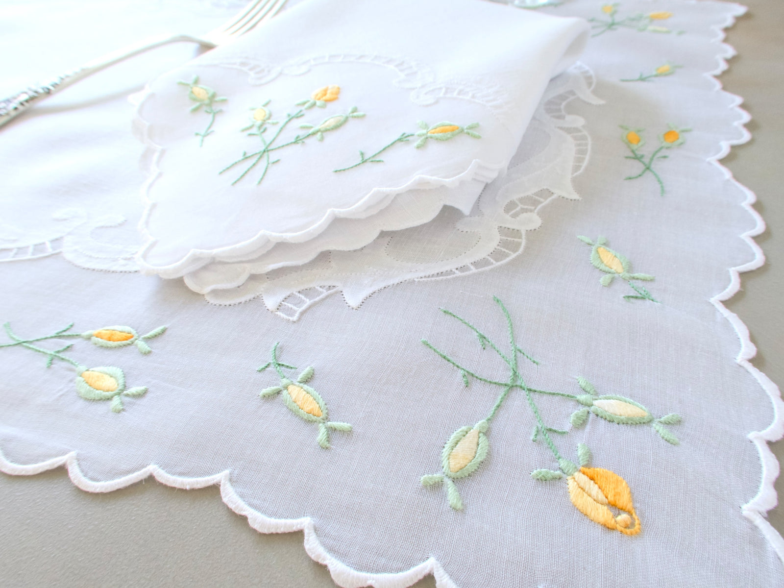 Close-up of vintage Madeira placemat corner with yellow rosebud sprigs and scalloped organdy border​​​​​​​​​​​​​​​​
