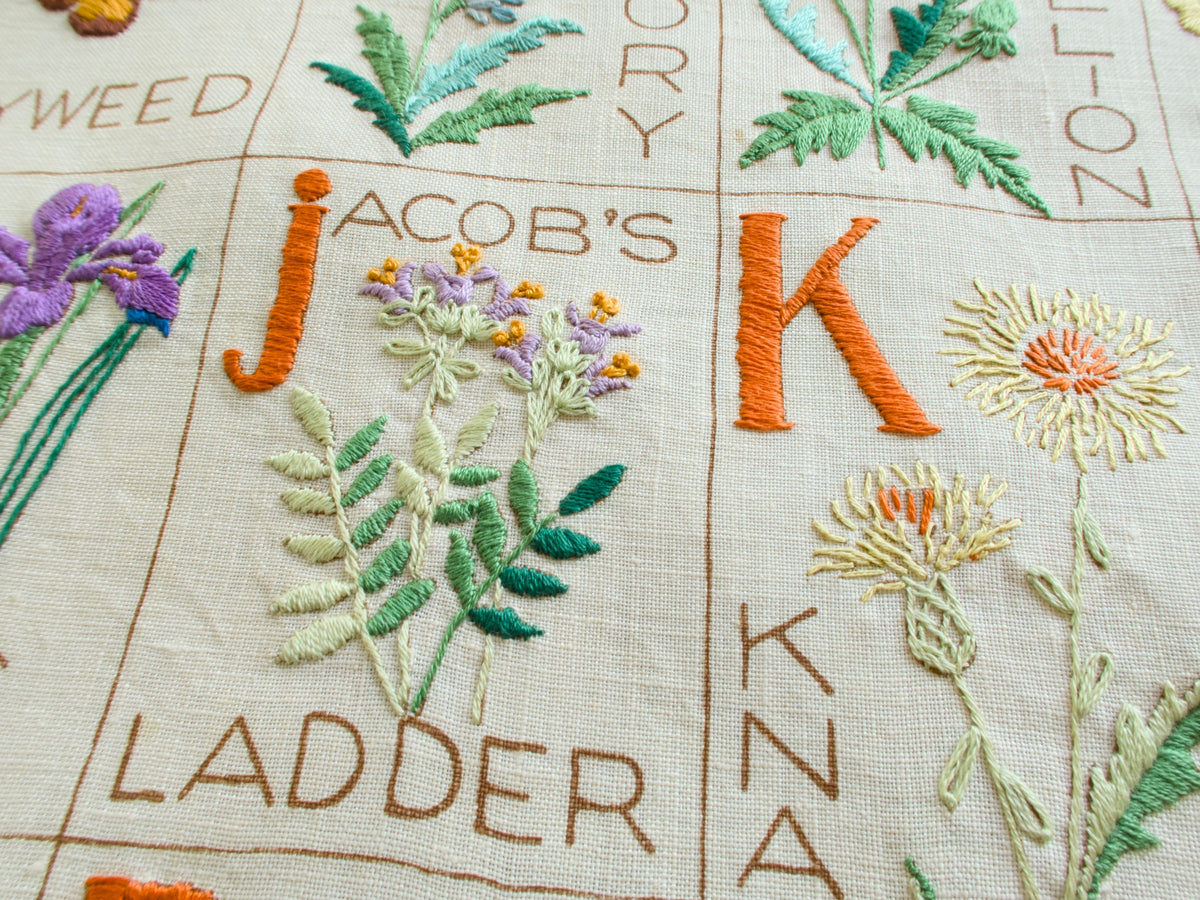 Detail of vintage botanical alphabet sampler showing Jacobs Ladder flower and embroidered lettering.