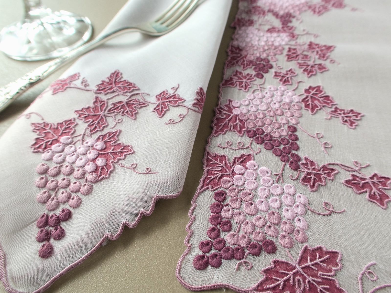 Vintage Marghab Vineyard linen napkin with hand embroidered grapes beside a placemat, a silver fork and a crystal glass