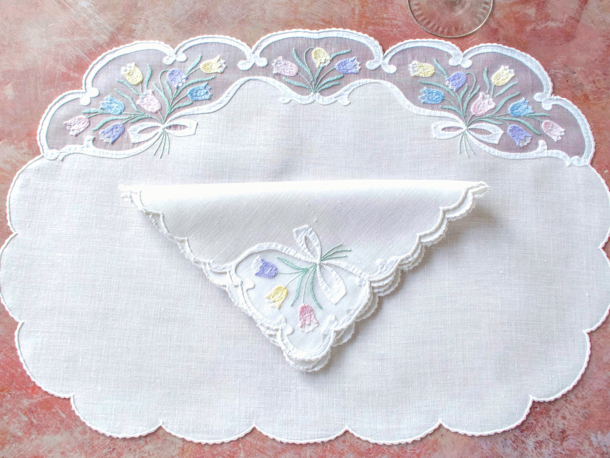 Vintage Madeira oval placemat with folded napkin showing tulip appliqué in organdy window and scalloped linen border.
