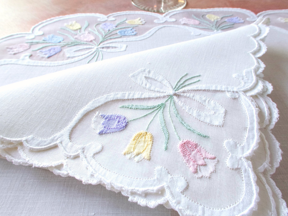 Detail of vintage Madeira oval placemat border showing pastel tulip embroidery in organdy windows on white linen napkin.