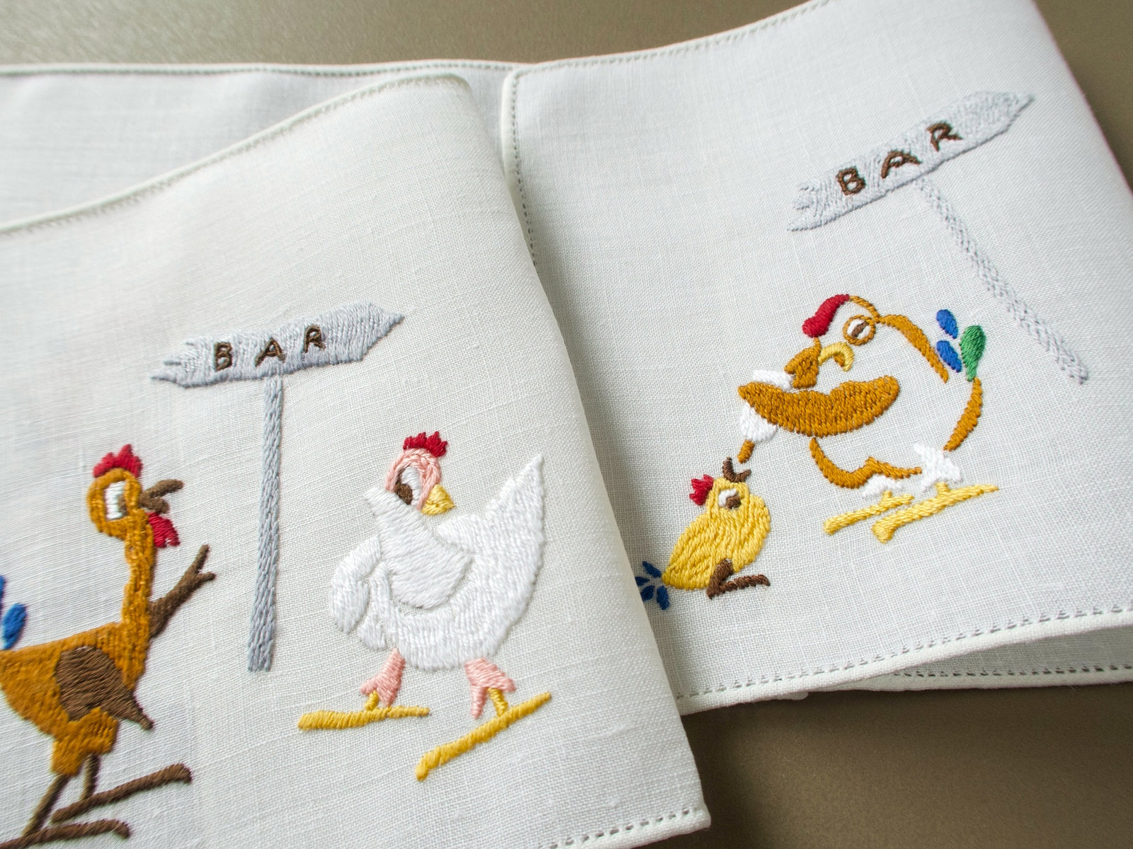 Vintage Rapisardi linen cocktail napkins folded to show hens flirting at the bar and a bleary-eyed hen feeding a bottle to a chick
