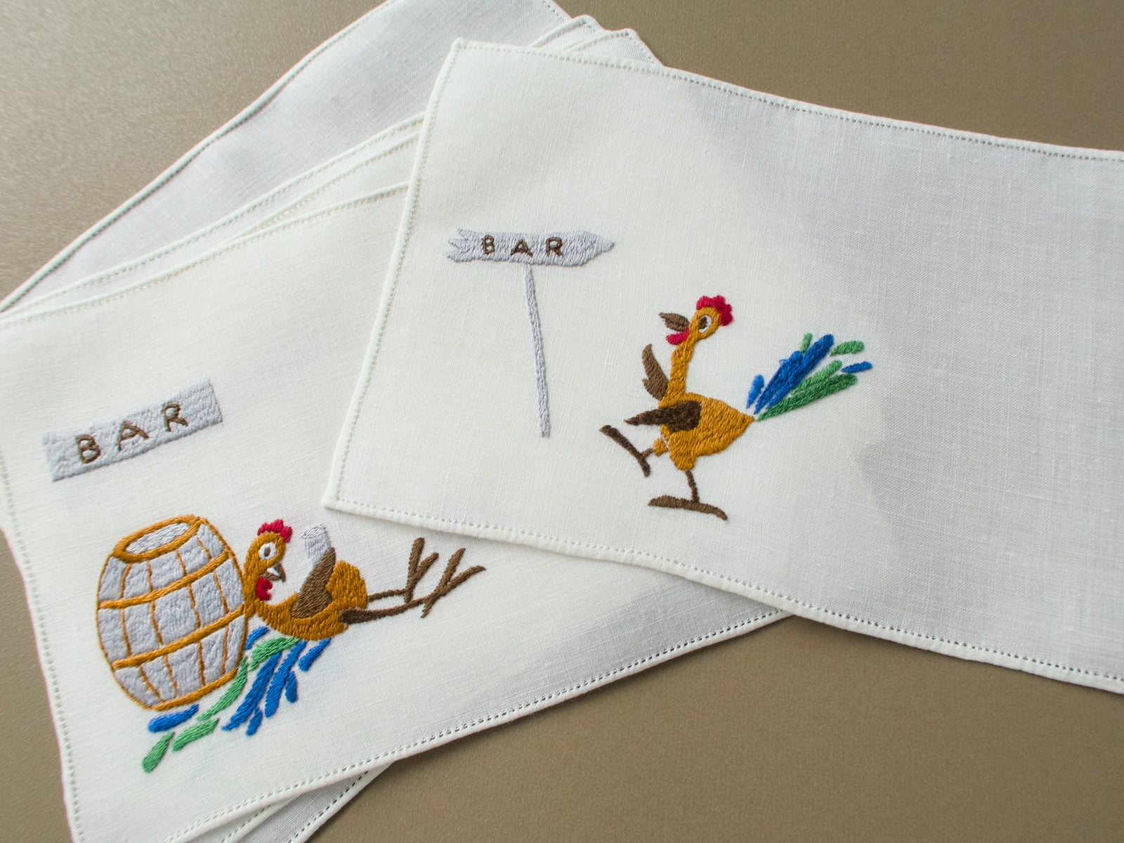 Two vintage Rapisardi linen cocktail napkins stacked to show hemstitched edges and embroidered roosters