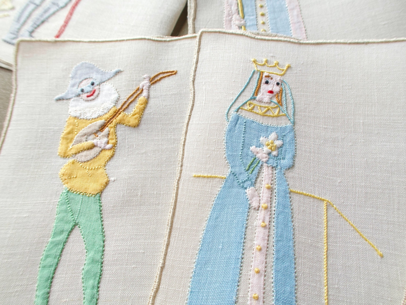 Vintage Madeira cocktail napkins with an appliqué joker playing a lute beside a queen holding a lily