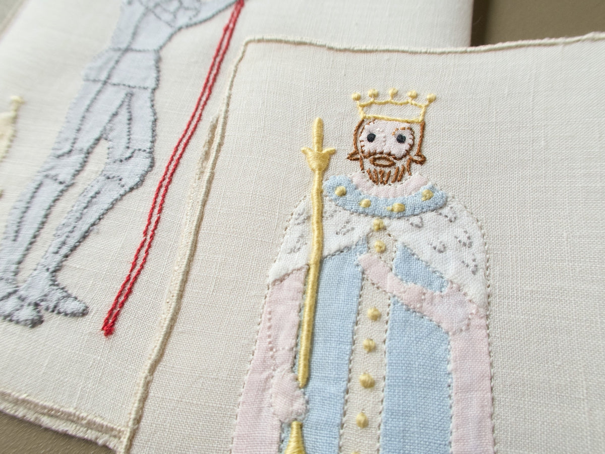 Close view of an appliqué king with a crown and scepter in an ermine collar on a vintage Madeira cocktail napkin