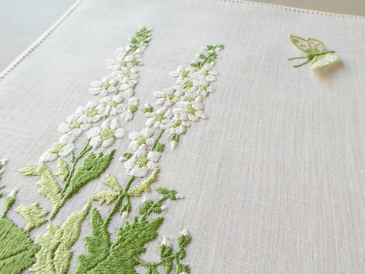 Close-up of vintage Rapisardi semi-sheer linen tray cloth hand embroidered in Italy with white delphinium spires and layered green foliage