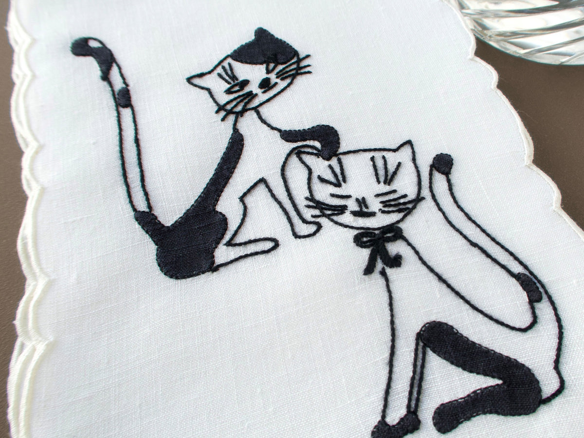 Closeup of a vintage Madeira cocktail napkins with black cats hand embroidered on white linen, scalloped edges