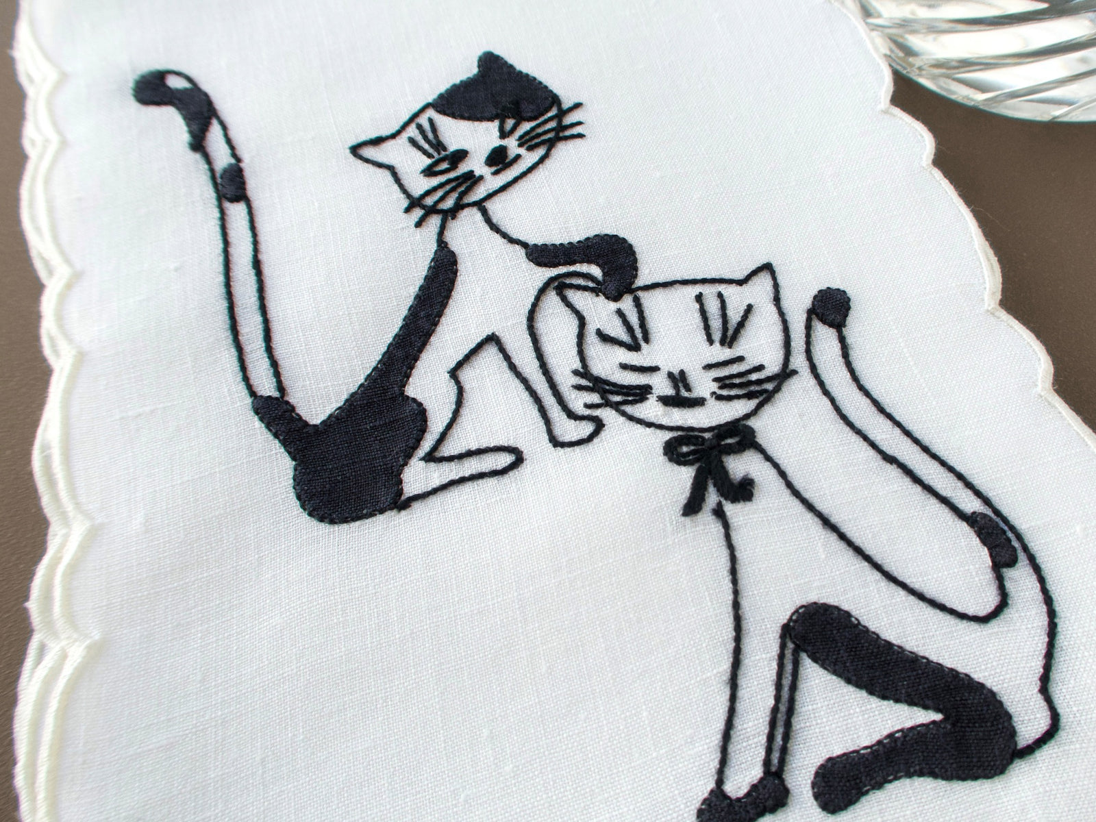 Closeup of a vintage Madeira cocktail napkins with black cats hand embroidered on white linen, scalloped edges