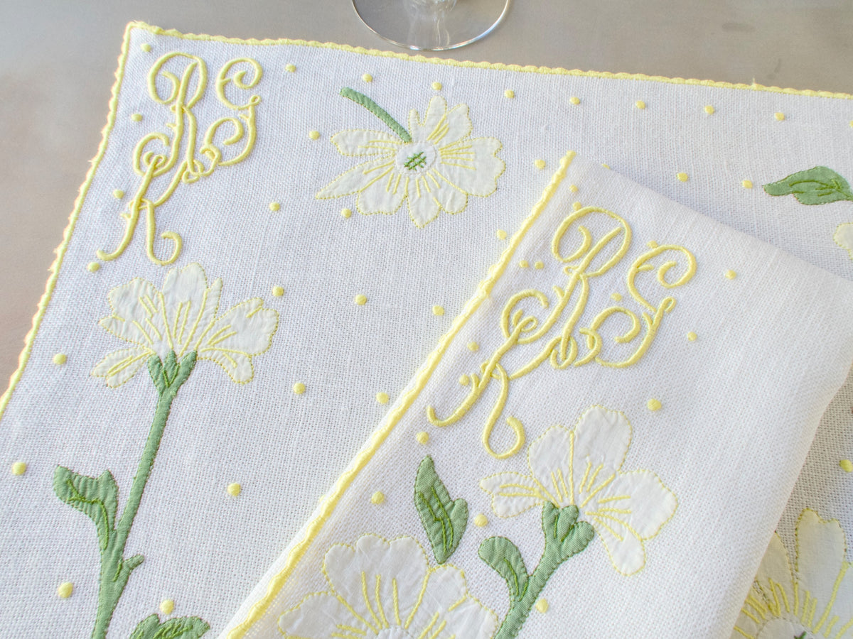 Detail of Madeira placemat corner showing daisy motif, dot embroidery, and yellow caseado bastido edging