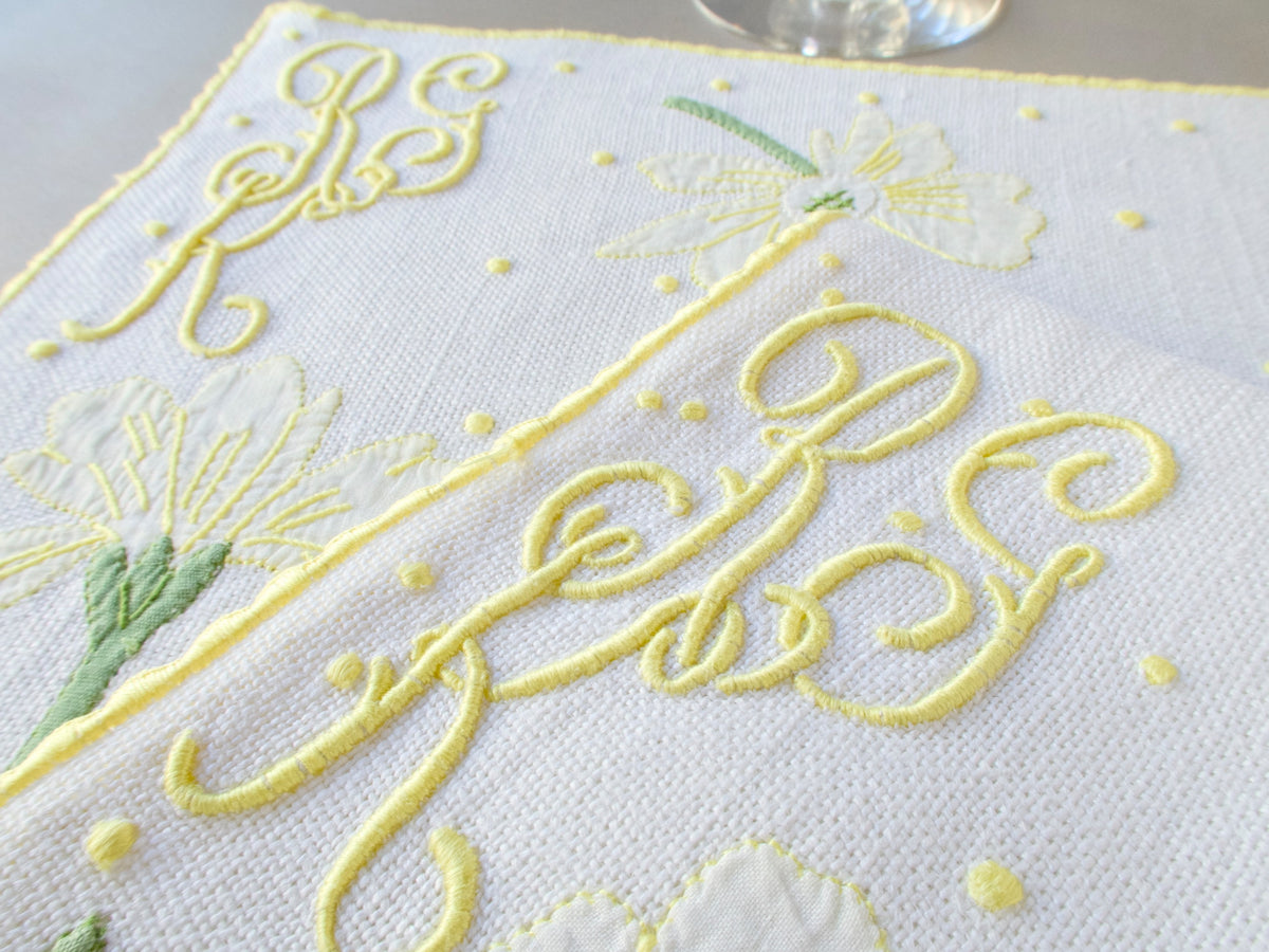 Close-up of elaborate cursive yellow monogram hand embroidered in Madeira on white textured linen​​​​​​​​​​​​​​​​