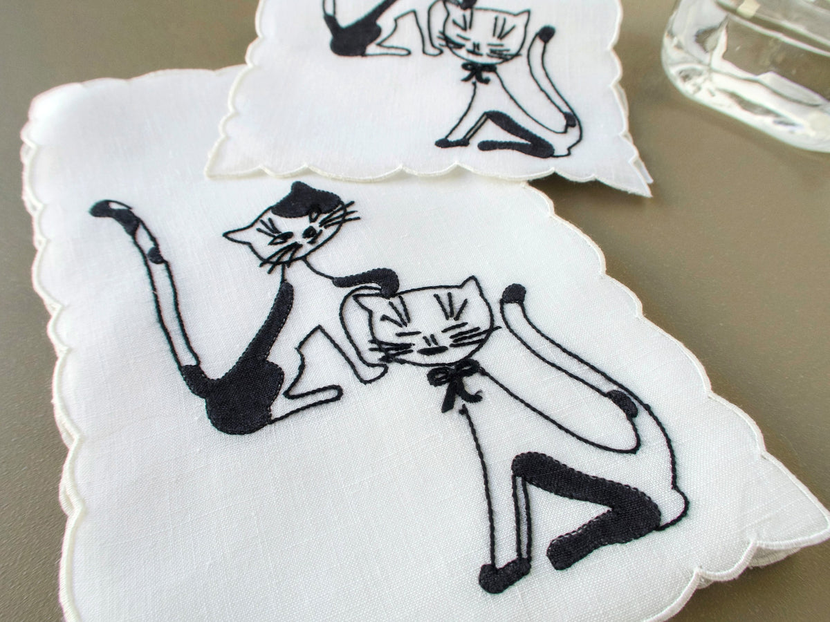 Two vintage Madeira cocktail napkins with black cats hand embroidered on white linen, scalloped edges