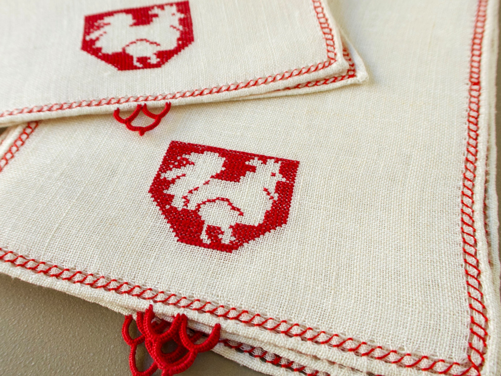 Single vintage Italian Assisi cocktail napkin on semi-sheer linen with a rooster in a crest, red edging and a lace embellishment