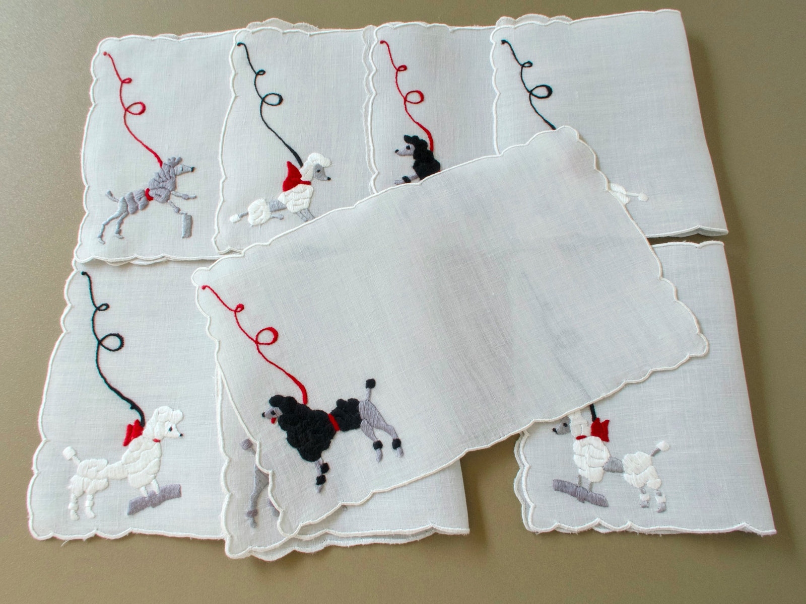 Eight vintage Madeira cocktail napkins with one laid flat over the others, showing a black poodle and the plain linen