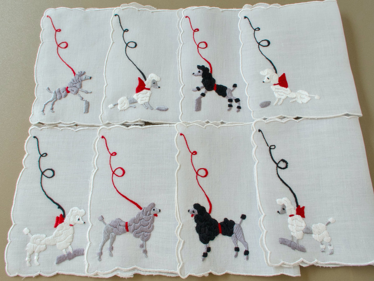 Eight vintage Madeira cocktail napkins laid out in two rows, each with a hand embroidered poodle on a looping leash