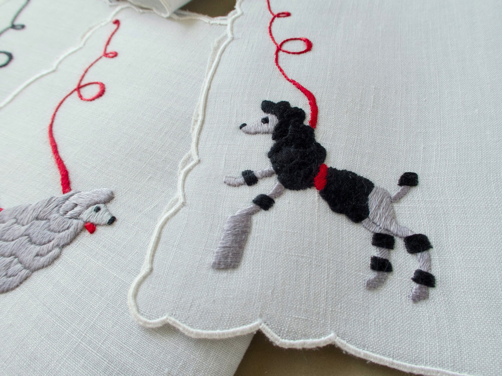 Close view of a black poodle leaping on a hand embroidered Madeira cocktail napkin with a scalloped edge