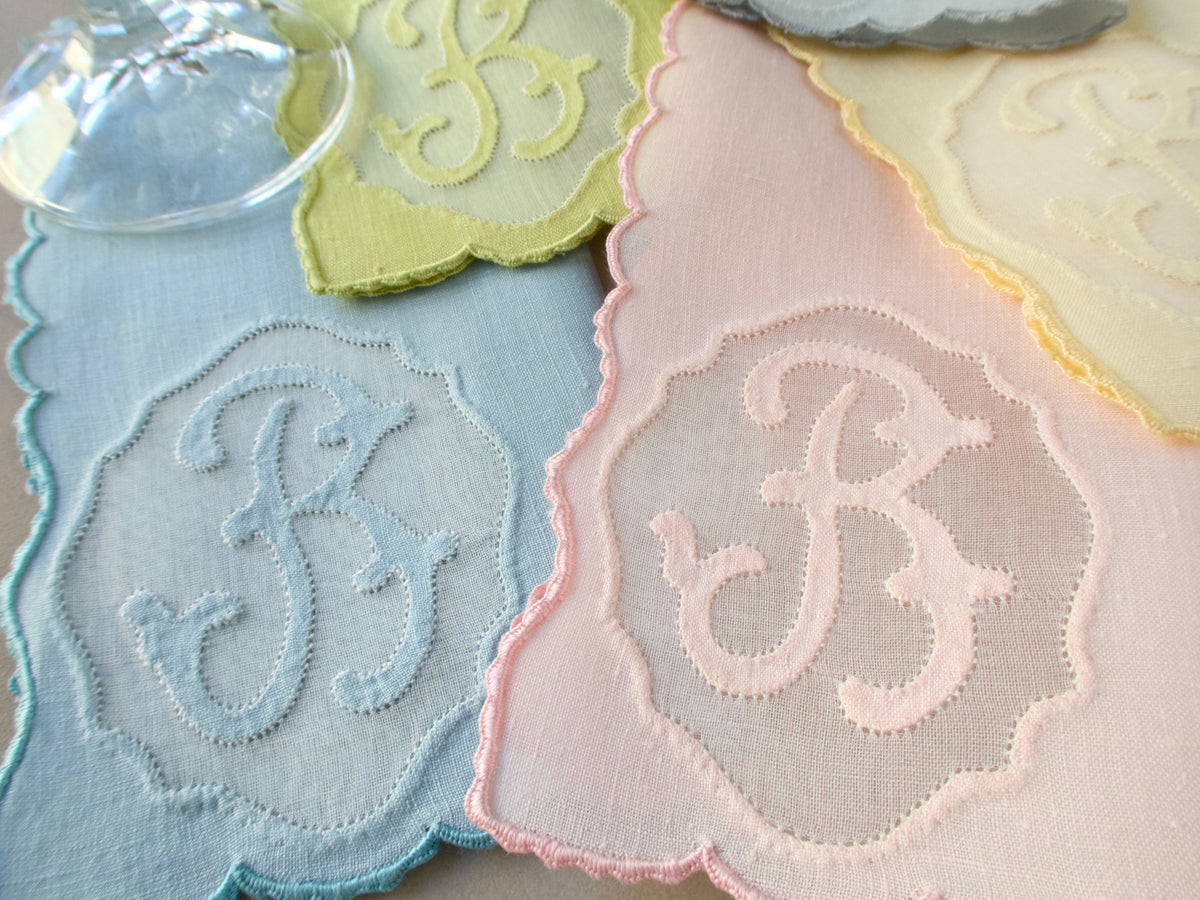 Close-up of vintage Madeira Irish linen cocktail napkins hand embroidered with cursive “B” monogram appliquéd in organdy window, in pink and white pastels with scalloped caseado bastido edging