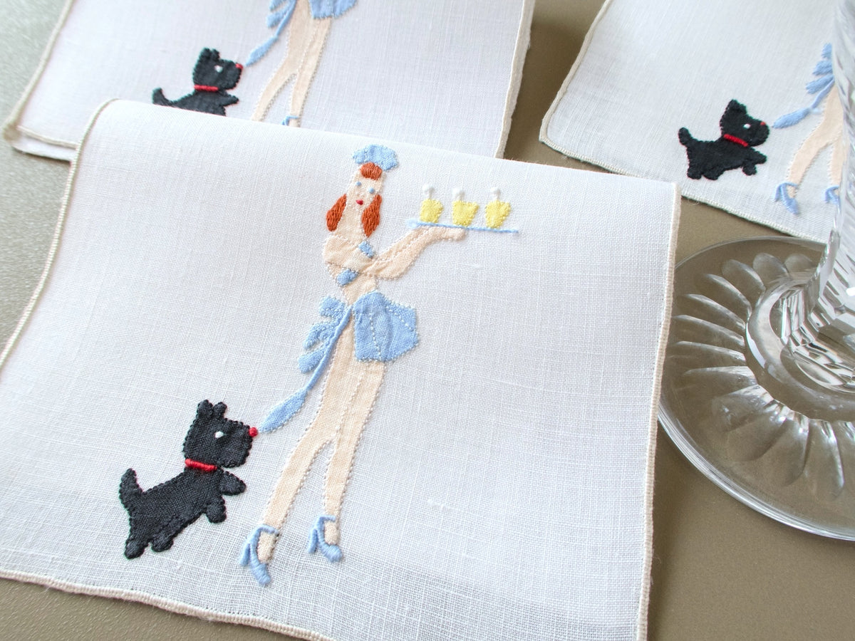 Vintage Madeira linen cocktail napkins embroidered with a black dog tugging a waitress’s blue apron tie as she carries drinks.
