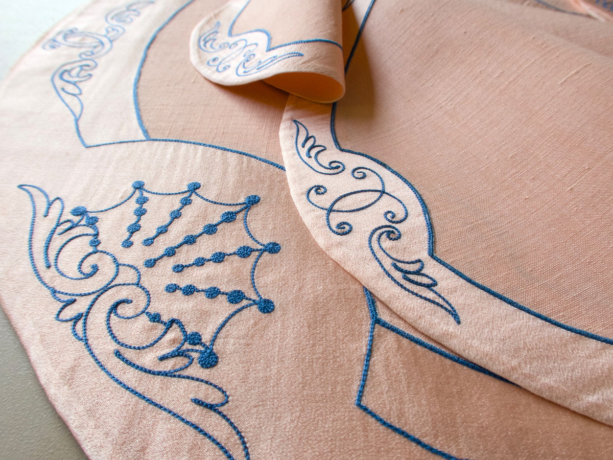 Close-up of vintage French Cornely embroidery showing blue chandelier and scrollwork motif on salmon silk and linen centerpiece