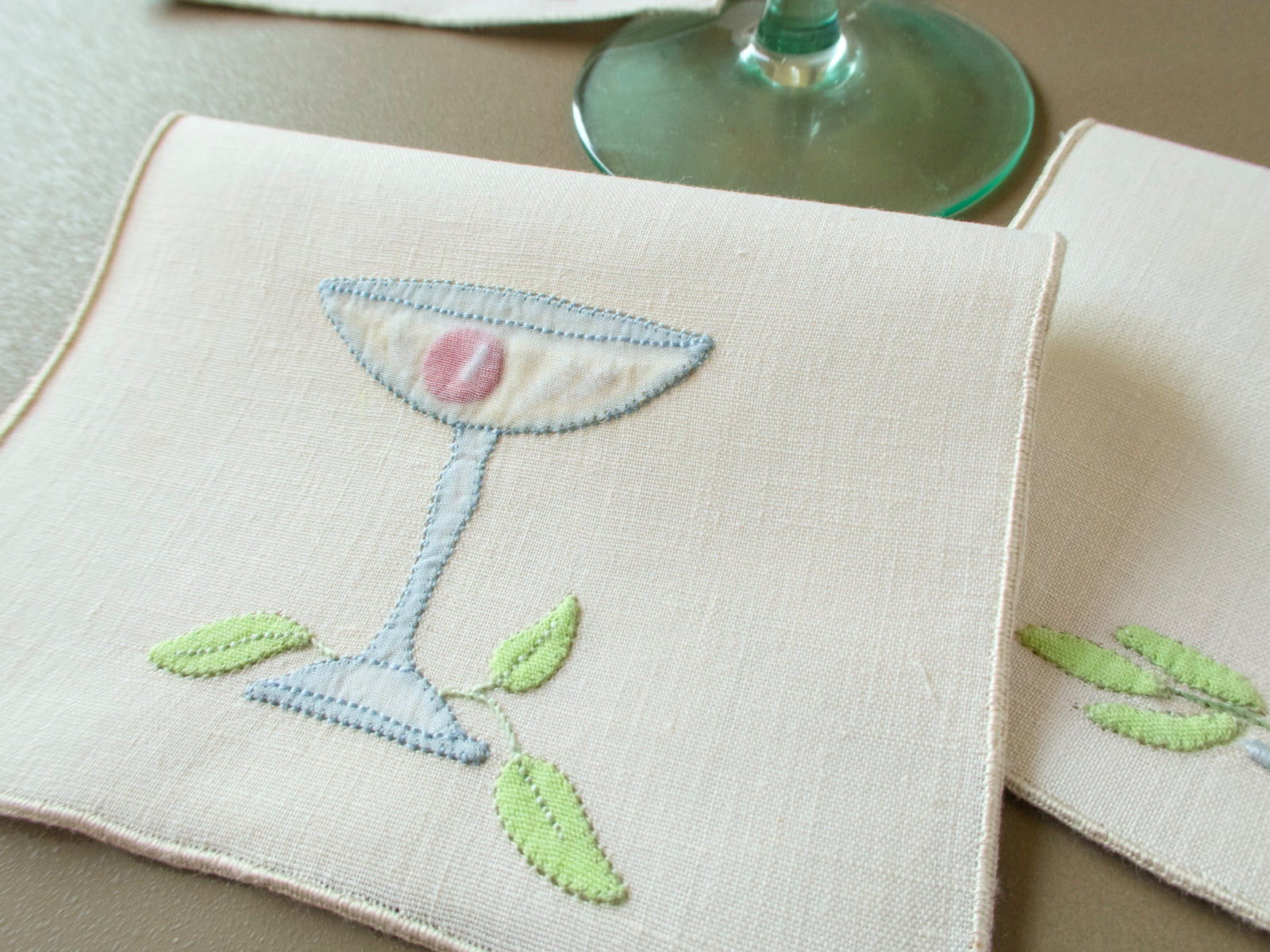 Vintage Madeira cocktail napkin with an appliquéd coupe glass, garnish and leaves beside a stemmed glass