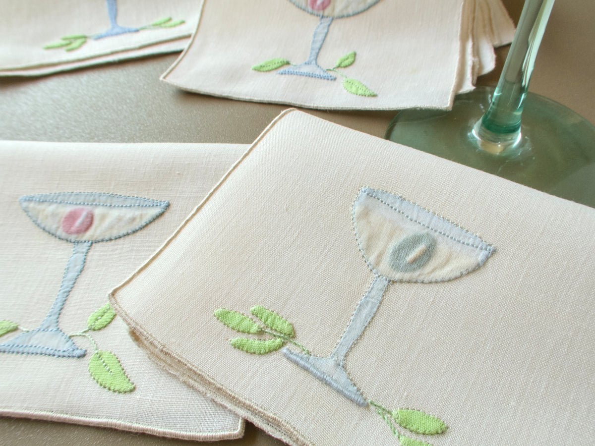 Vintage Madeira cocktail napkins with appliquéd glasses and garnishes fanned out beside a stemmed glass
