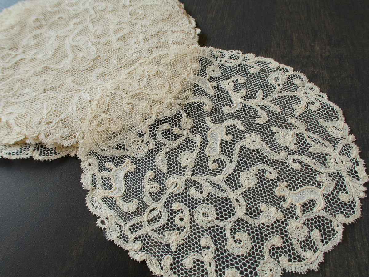 Two antique bobbin lace coasters, one resting on the other, showing the scrolling pattern