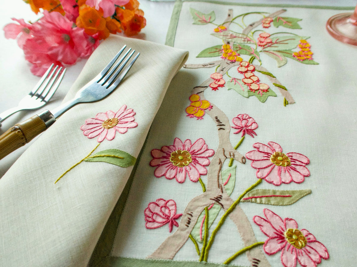 A set of vintage Italian placemats with floral embroidery, accompanied by napkins and cutlery, displayed on a table.