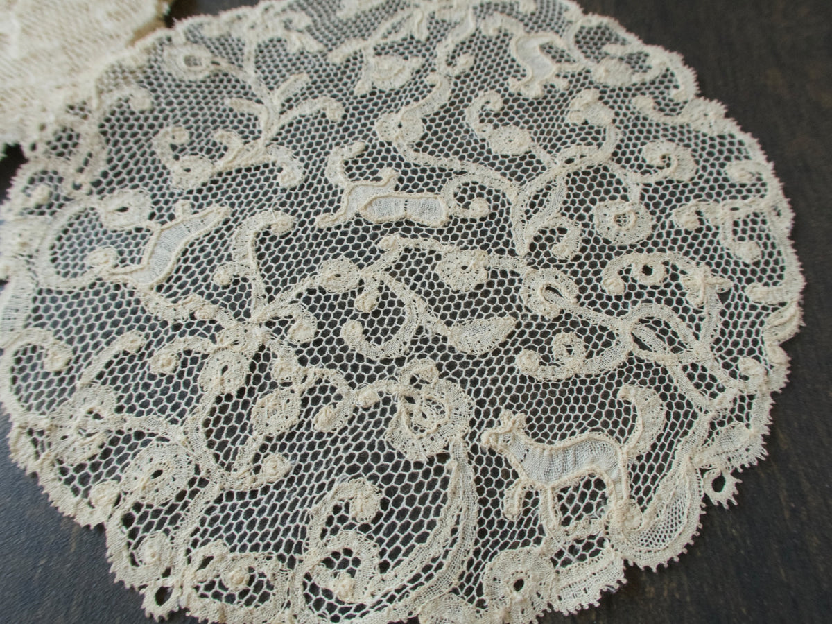 Close view of an antique handmade bobbin lace coaster with tiny animals among meandering scrolls