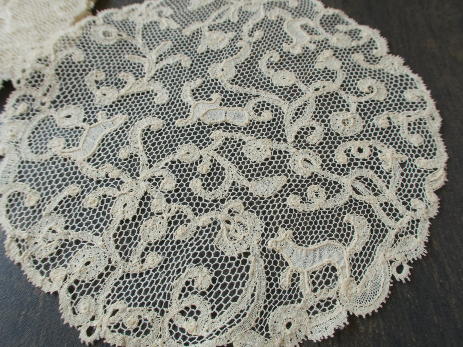 Close view of an antique handmade bobbin lace coaster with tiny animals among meandering scrolls