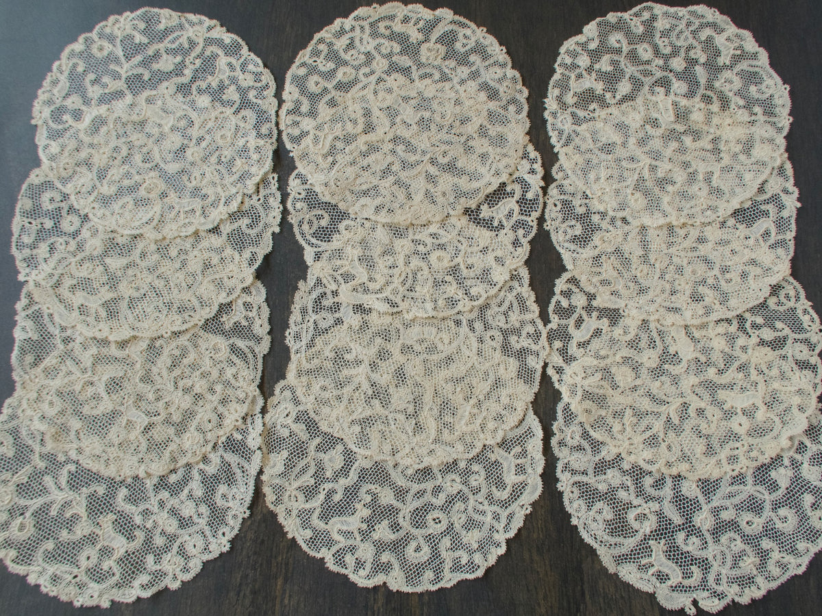Three stacks of antique handmade bobbin lace coasters, set of 12, on a dark background