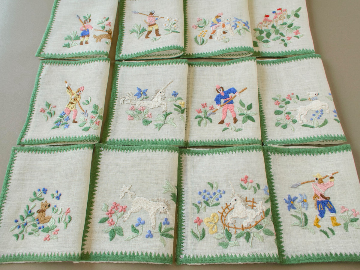 Set of 12 folded vintage Baroness Rapisardi Hunt of the Unicorn cocktail napkins in three rows, each hand embroidered in punto stuoia with a different scene of unicorns, hunters, hounds and a castle